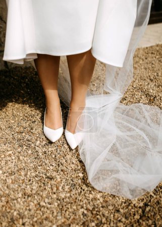 Foto de Patas de novia en zapatos blancos sobre grava, con velo. - Imagen libre de derechos
