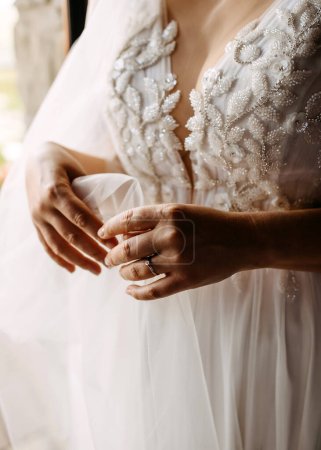 Foto de Una novia sosteniendo su velo, usando un anillo de compromiso de diamantes, a la luz del sol, de cerca. - Imagen libre de derechos