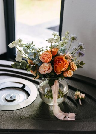 Téléchargez les photos : Bouquet de mariée en vase de verre sur table avec ruban, près de la fenêtre. - en image libre de droit