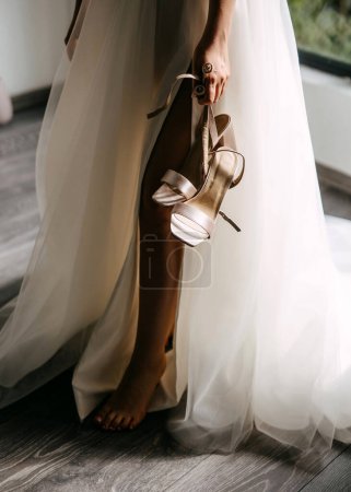 Photo for Bride standing barefoot, holding elegant wedding shoes. - Royalty Free Image
