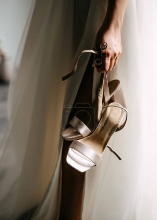 Photo for Bride holding elegant wedding shoes, closeup. - Royalty Free Image