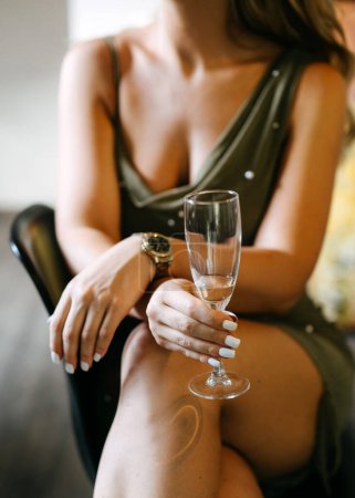Téléchargez les photos : Gros plan d'une femme, vêtue d'une mini robe chic, tenant un verre de champagne. - en image libre de droit