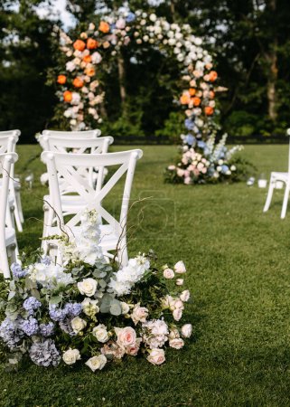 Foto de Configuración de la boda al aire libre con arco floral. Pasillo de boda con sillas de madera blanca. - Imagen libre de derechos