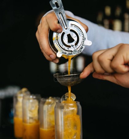 Photo for Bartender pouring an orange drink through a strainer into a glass. - Royalty Free Image