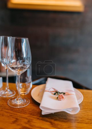 Foto de Elegante mesa con copas de vino y un plato con una servilleta blanca y una pequeña rosa rosa colocada en ella. - Imagen libre de derechos