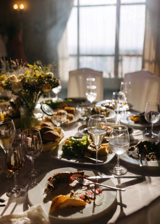 Festive banquet aftermath : table ensoleillée avec des restes d'un repas et du vin dans des verres.