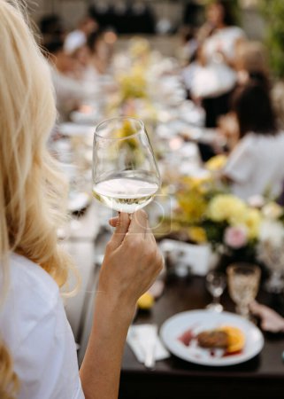 Téléchargez les photos : Une femme tenant un verre de vin, avec une table de banquet en arrière-plan. - en image libre de droit