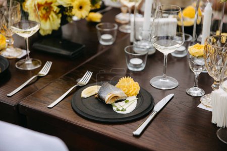 Téléchargez les photos : Dîner élégant avec assiette de poisson, citron et purée de pommes de terre sur assiette noire, fond floral jaune. - en image libre de droit