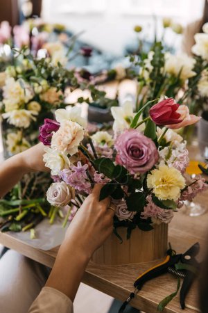 Foto de Una vista de cerca de las manos organizando un ramo de varias flores en una mesa de taller floral. - Imagen libre de derechos