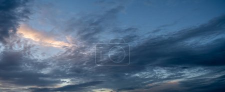 Panorama of only sky with late day clouds in shades of blue with a few slight red white clouds and with patches of blue sky.