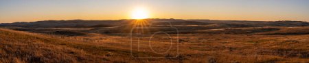 Foto de Largo panorama de una puesta de sol sobre una pradera de otoño de oro. Las pequeñas colinas se destacan por el sol del último día. El sol aparece como una estrella solar. - Imagen libre de derechos