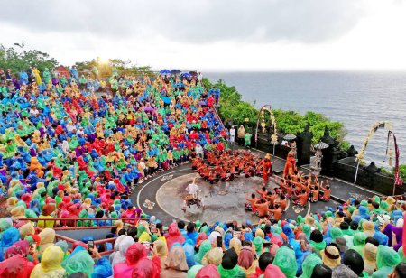Foto de Bali, Indonesia - 27 de enero de 2023: Kecak y Fire Dance, perfumándose en el escenario del templo de Uluwatu durante el día lluvioso, mira a todo el público usar el impermeable durante la actuación - Imagen libre de derechos
