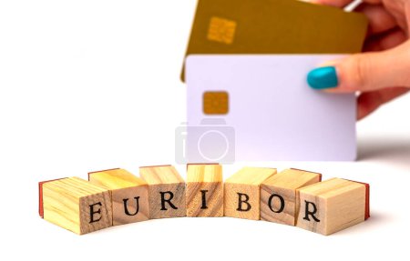 Photo for Word EURIBOR Is Written In Wooden Letters On White Background, Behind Woman Hand With Two Bank Card. Copy paste. Concept of Decreasing Purchasing Power. High quality photo - Royalty Free Image