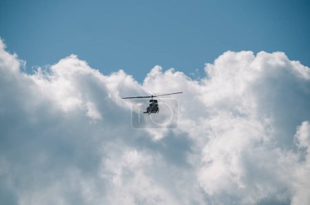 Foto de Kerkyra, Grecia - 09 24 2022: Alto en el cielo sobre el fondo de las nubes, un helicóptero blanco vuela sobre la isla de Corfú. Volar un helicóptero es un trabajo difícil. Foto de alta calidad - Imagen libre de derechos