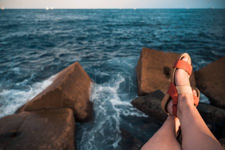 Téléchargez les photos : Gros plan de jambes féminines en sandales rouges sur fond flou de brise-lames et de mer avec des yachts blancs. Le concept de détente et de plaisir de la vie. Photo de haute qualité - en image libre de droit
