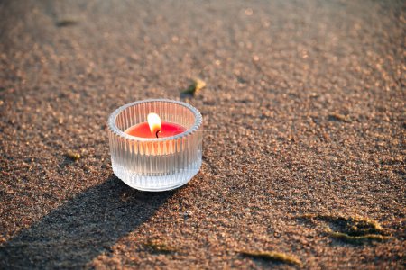 Téléchargez les photos : Une bougie rouge brûle sur la plage. Les bougies sur la plage peuvent être associées à l'ambiance festive et servir à décorer des événements et des fêtes sur la plage. Photo de haute qualité - en image libre de droit