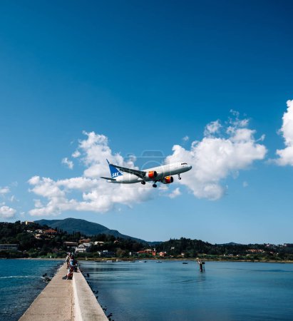Foto de Kerkyra, Grecia - 09 24 2022: El avión de SAS Scandinavian Airlines aterriza en el aeropuerto de Corfú. Bajo el avión, el lugar más turístico de las islas es un puente para fotografiar a los turistas. Foto de alta calidad - Imagen libre de derechos