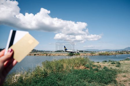 Foto de Kerkyra, Grecia - 09 24 2022: Ryanair Plane On Corfu Airport. En primer plano, fuera de foco, hay una mano de mujer que sostiene tarjetas bancarias, como señal de un viaje aéreo económico. Foto de alta calidad - Imagen libre de derechos
