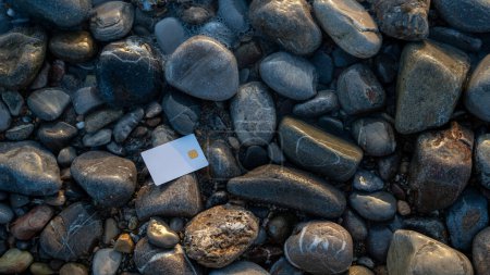 Photo for White bank card placed on smooth gray stones, symbolizing the intersection of money and nature. copy space. High quality photo - Royalty Free Image