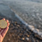 Woman has a gold coin with a Bitcoin symbol in her hand, against the backdrop of the sea. High quality photo