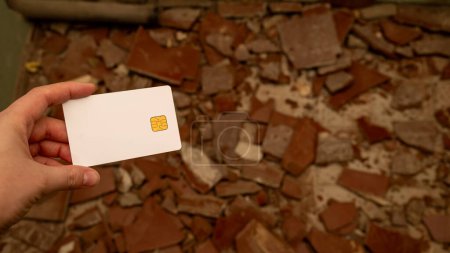Womans hand with a bank card against the background of pieces of broken tiles on the floor. The concept of starting repairs and the high cost of repairs. High quality photo