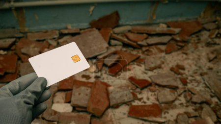 womans hand in construction gloves with a bank card against the background of pieces of broken tiles on the floor. The concept of starting repairs and the high cost of repairs. High quality photo