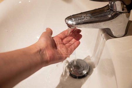 Eine Person benutzt einen Klempner, ein Waschbecken, um sich die Hände mit Wasser und Flüssigkeit zu waschen, während sie mit ihren Fingern und Daumen auf der Arbeitsplatte Gesten macht.