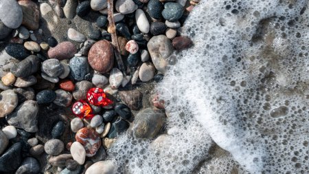 Red playing dice among gray stones and foam from the sea wave. High quality illustration