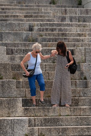 Photo for Cape Town, South Africa. 2023. Elderly person getting assistance from a female carer in walking down very steep steps at a tourist attraction. - Royalty Free Image