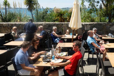 Foto de Herm, Islas del Canal, Reino Unido. 11 de junio 2023. Los turistas disfrutando de un almuerzo al aire libre en un restaurante de Herm Island la vista es hacia Guernsey otra isla del Canal. - Imagen libre de derechos