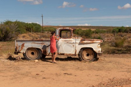 Photo for South Africa. 16/02/2024. Attractive woman getting into an old rusty American car on the roadside in the Swartland region of South Africa. - Royalty Free Image