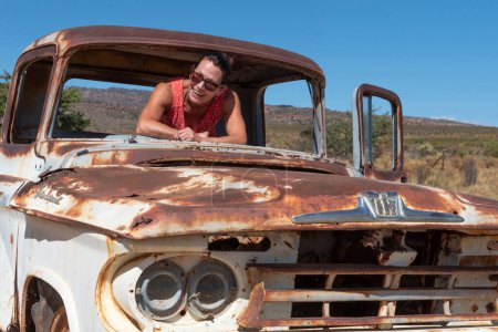 Photo for South Africa. 16/02/2024. Attractive woman posing with an old rusty American car on the roadside in the Swartland region of South Africa. - Royalty Free Image