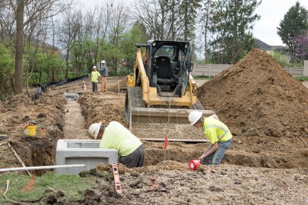 Photo for Dayton, Ohio - April 9, 2024: Construction workers work in stone aggregate in drainage trench as part of housing development drainage system. - Royalty Free Image
