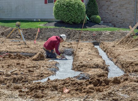 Téléchargez les photos : Dayton, Ohio - 25 avril 2024 : Un ouvrier de la construction de maçonnerie lisse le béton en pied de page d'un nouveau lotissement. - en image libre de droit