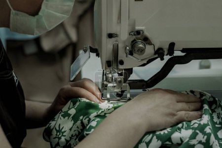 Foto de El proceso de coser botones para un vestido por un artesano; equipo de seguridad en la producción de ropa de mujer; una mujer trabaja en la costura de ropa - Imagen libre de derechos