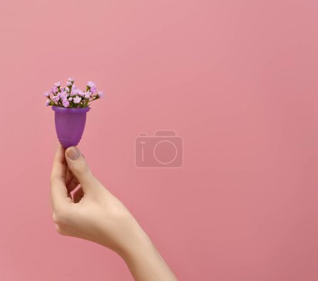Photo for Female hand holding menstrual cup  filled with flowers  on pink background, woman wellbeing concept - Royalty Free Image