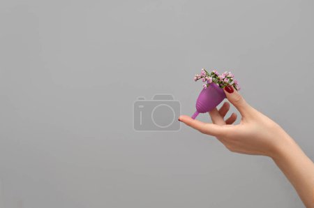 Photo for Female hand holding menstrual cup filled with flowers  on gray background, woman wellbeing concept - Royalty Free Image