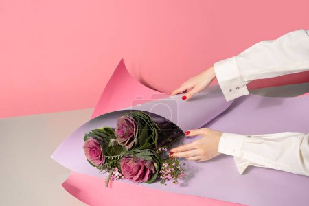 Photo for Female hands wrapping the bouquet of flowers in paper on pink background - Royalty Free Image