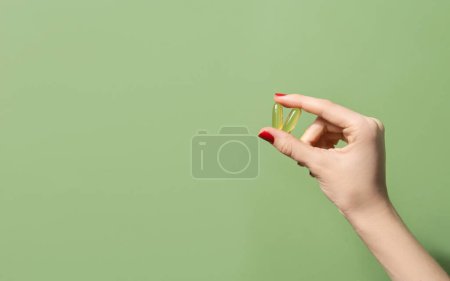 Photo for Female hand holding two oil capsules on green background. Wellbeing concept - Royalty Free Image