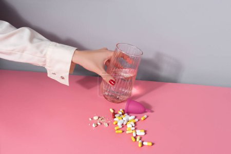 Photo for Female hand putting a glass of water. handful of pills and menstrual cup on a table. Woman Well-being concept - Royalty Free Image