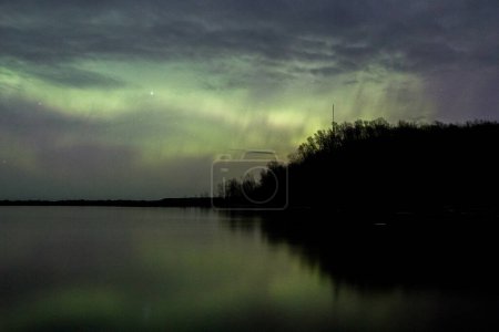 Northern lights reflect in the mouth of the black river in northern Michigan on a partly cloudy night.
