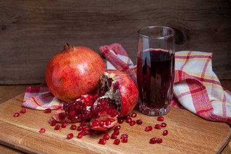 Komposition aus reifem roten Granatapfel und einem Glas frischem rubinroten Saft auf einem hölzernen Hintergrund. Nahaufnahme von Rubinkernen Granatapfelfrüchten und süßem frischen Saft im Glas