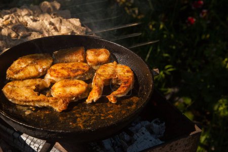 Téléchargez les photos : Poêle avec steak de poisson à frire sur le feu. Cuisine extérieure. Barbecue d'été et vacances - en image libre de droit