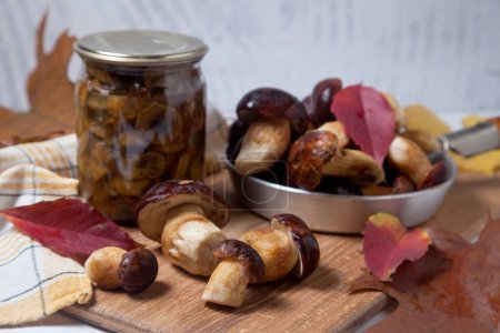 Autumn composition of several Imleria Badia or Boletus badius mushrooms commonly known as the bay bolete and vintage pan with mushrooms on wooden cutting board with vivid autumn leaves. Edible and pored fungus has velvety dark brown or chestnut color