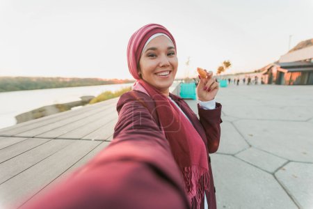 Foto de Mujer en abaya grabando video en la cámara selfie mientras pasa tiempo en la calle - Imagen libre de derechos