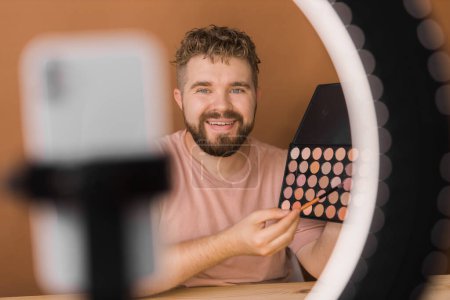 Photo for Male beauty blogger doing his make up and recording a video lesson his with mobile phone - vlog, diversity and video blog - Royalty Free Image
