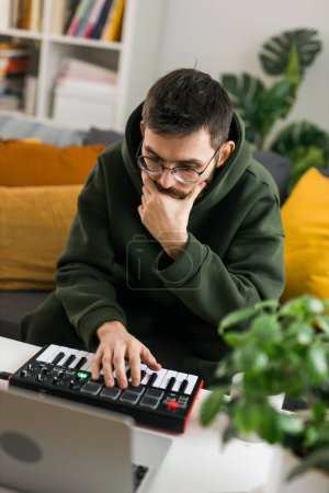 Photo for Recording electronic music track with portable midi keyboard on laptop computer in home studio. Producing and mixing music, beat making and arranging audio content with professional audio devices - Royalty Free Image