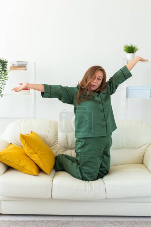 Téléchargez les photos : Fun esprit femme porter un pyjama elle assis sur le canapé utilisation repos se détendre passer du temps dans le salon salon maison dans sa propre salle de réveil concept - en image libre de droit