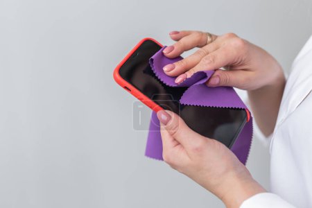 Téléchargez les photos : Élimination des germes. Nettoyage de l'écran du smartphone avec un chiffon en fibre de poussière de saleté et d'autres facteurs externes. Soins mobiles - en image libre de droit