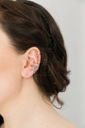 Foto de Recortado primer plano de una mujer joven con manguitos asimétricos de plata. Mujer con orejeras de metal, vista lateral. - Imagen libre de derechos
